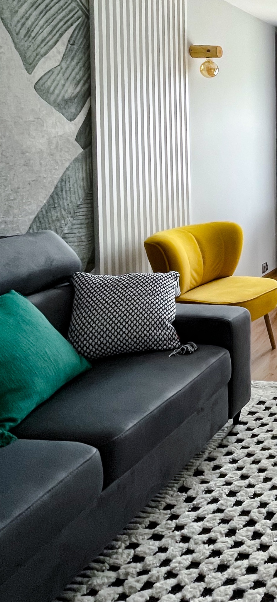 Stylowy salon we Wrocławiu: szara sofa z poduszkami, żółty fotel i wzorzysty dywan. Nowoczesne oświetlenie i dekoracje ścienne tworzą przytulną atmosferę.
