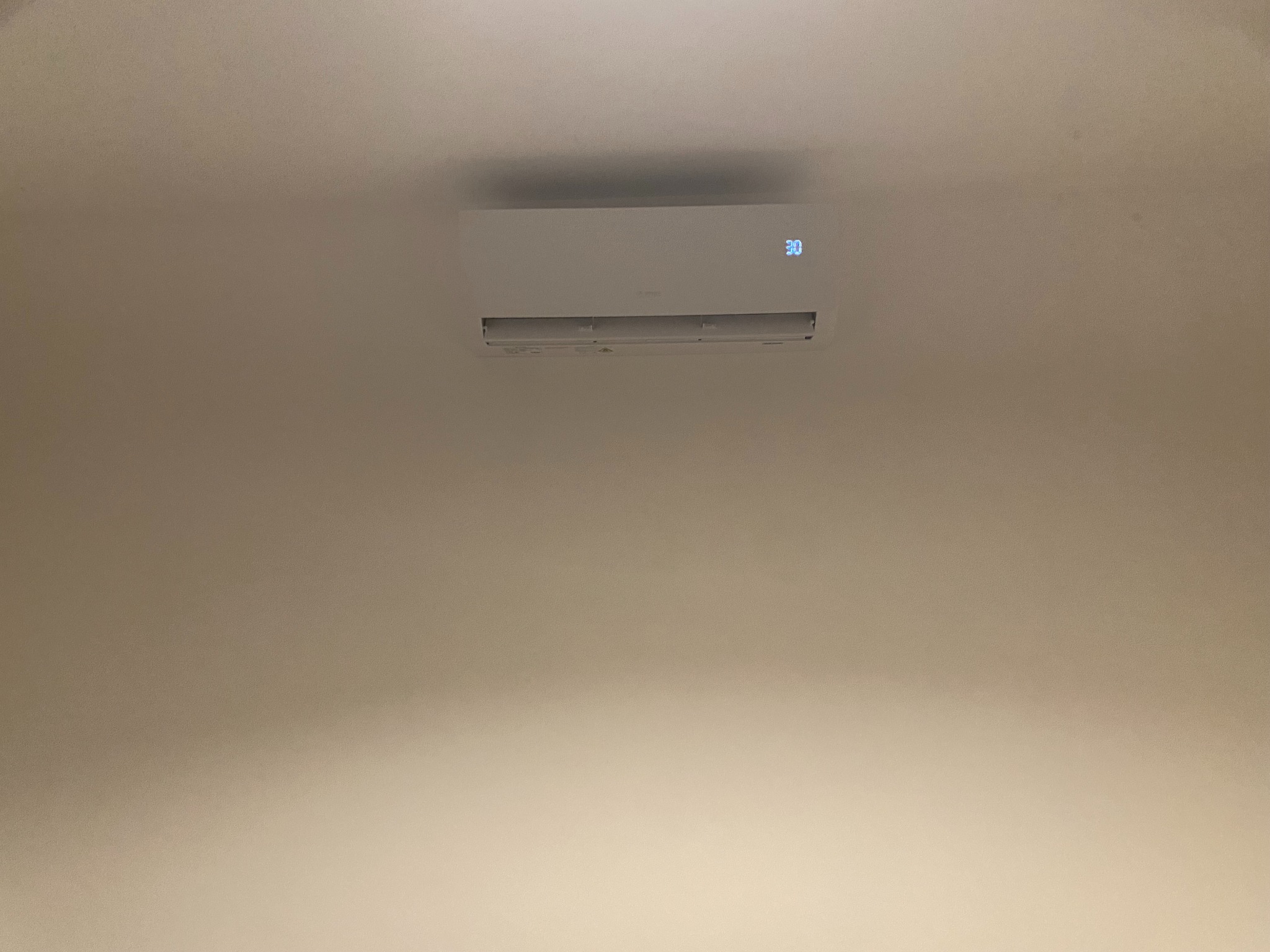 Biała klimatyzacja ścienna z wyświetlaczem temperatury 30 stopni, zamontowana na jasnej ścianie. Minimalistyczny design, widok od dołu.