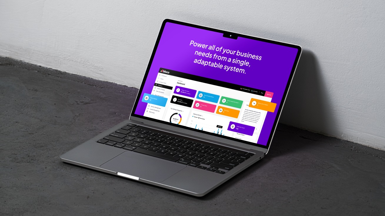Laptop wyświetlający interfejs użytkownika aplikacji biznesowej z fioletowym tłem i kolorowymi elementami graficznymi, ustawiony pod kątem na szarym tle.