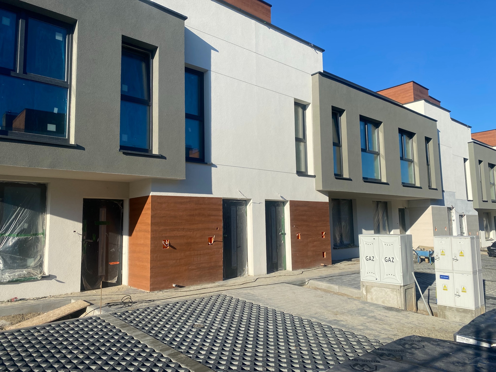 Nowe segmenty domów w Rzeszowie, w trakcie wykończenia, z widocznymi instalacjami gazowymi i częściowo wyłożonym podjazdem z ażurowych płyt.
