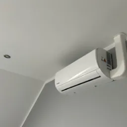 Biały klimatyzator Kaisa montowany na szarej ścianie w Bobrownikach. Widoczny fragment sufitu z oświetleniem punktowym i rura odprowadzająca.