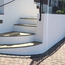 EVERCOAT KAROL KUMOR - Białe, otynkowane schody zewnętrzne z kamiennymi stopniami i czarną balustradą, prowadzące do domu, z widoczną kostką brukową na podjeździe.