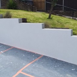 EVERCOAT KAROL KUMOR - Świeżo pomalowany, schodkowy murek elewacyjny na zewnątrz domu, z wiaderkiem farby i zabezpieczonym podłożem.