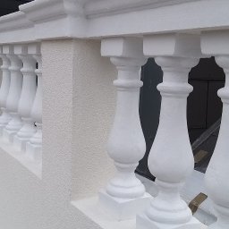 EVERCOAT KAROL KUMOR - Biała balustrada z kolumnami na balkonie po renowacji, widok z góry, szare dachy w tle.