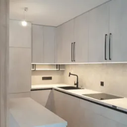 Nowoczesna kuchnia z szarymi szafkami, czarnymi uchwytami i oświetleniem LED pod szafkami. Widoczny piekarnik i czarny zlew. Minimalistyczny design.