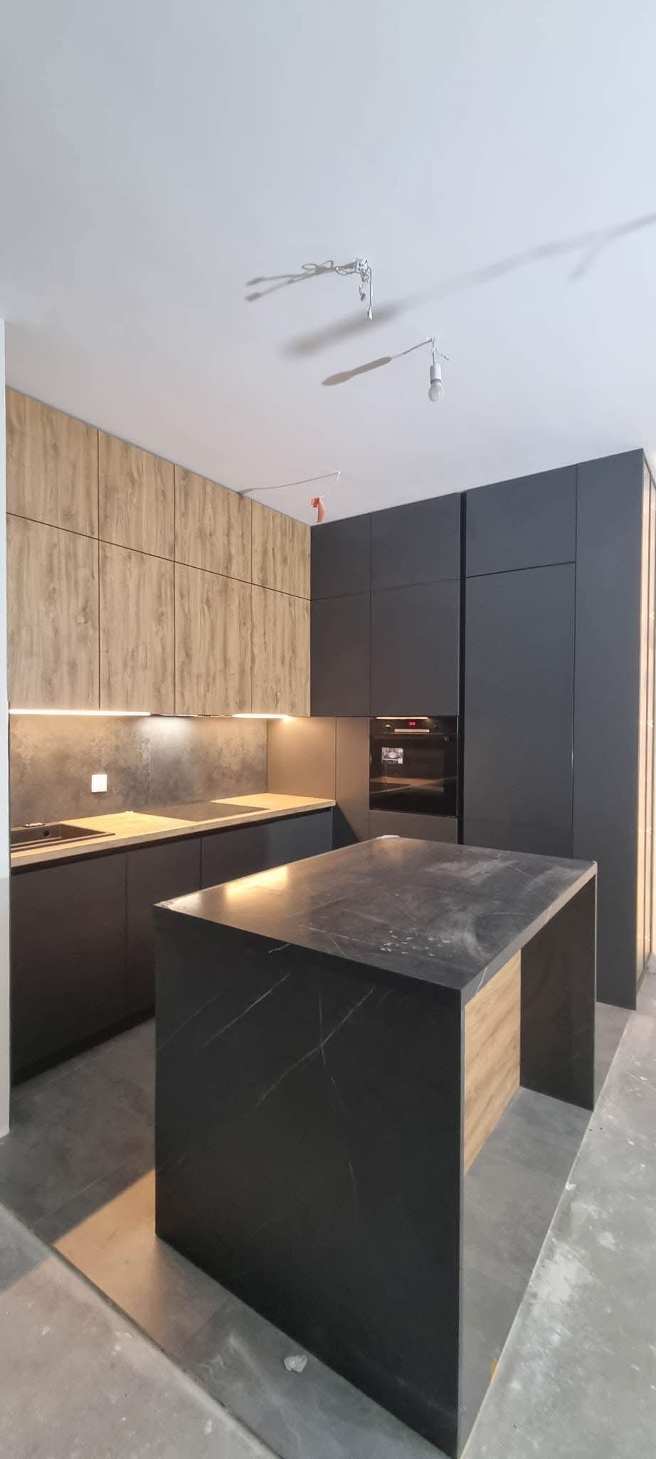 Nowoczesna kuchnia z wyspą o marmurowym blacie i drewnianymi szafkami górnymi, oświetlona ledami pod szafkami, z szarymi szafkami dolnymi i piekarnikiem w zabudowie.