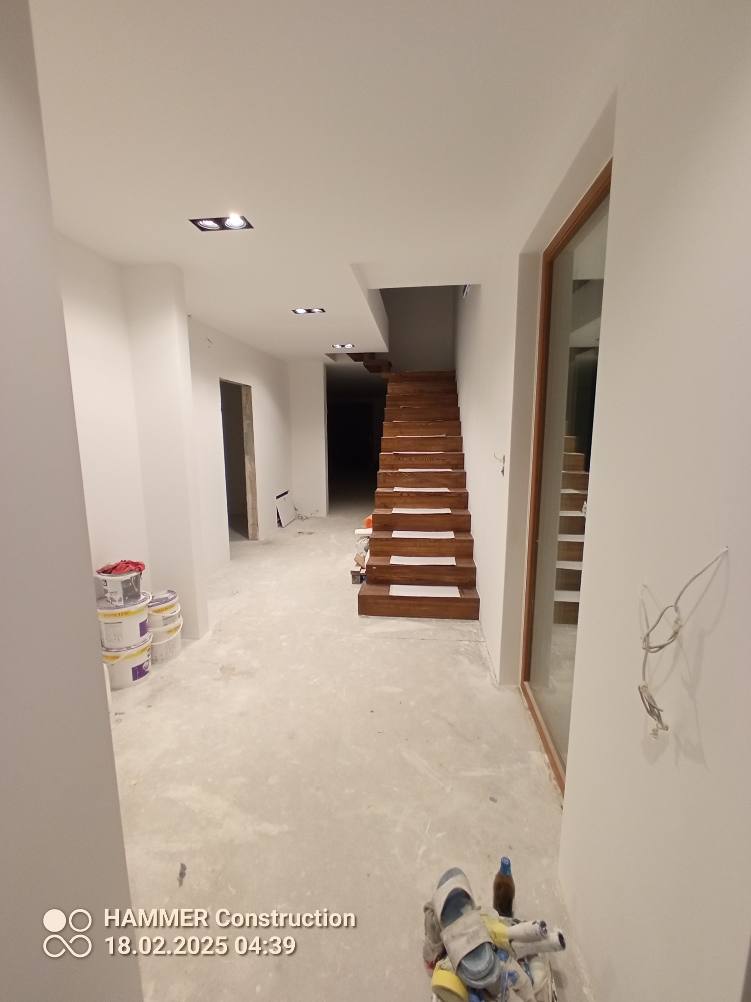 Wnętrze domu w Gnieznie po malowaniu ścian na biało, z widocznymi schodami i oknem. Ślady farby na podłodze sugerują trwające prace wykończeniowe.