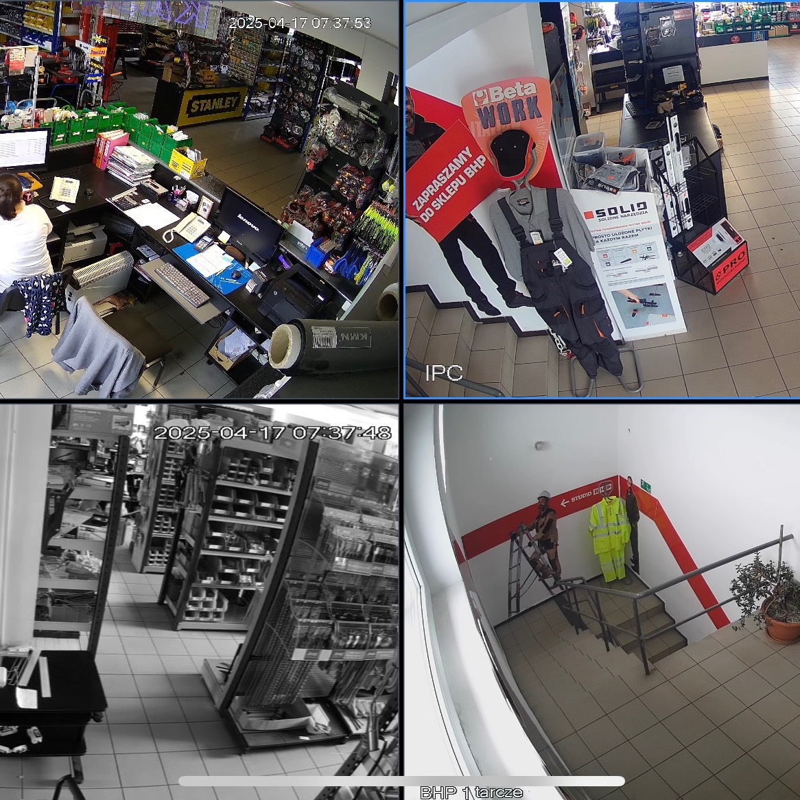 Zrzut ekranu z systemu monitoringu wizyjnego sklepu z narzędziami BHP, prezentujący jednocześnie kasę, ekspozycję odzieży roboczej i schody z pracownikiem na drabinie.