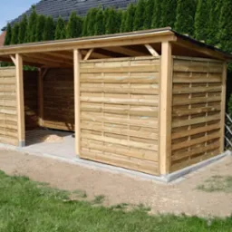 Drewniana wiata z ażurowymi ścianami, betonowa podstawa, widok z zewnątrz na tle zieleni.