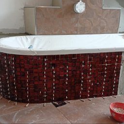 Daniel Kłosiński - Proces wykańczania wanny mozaiką z czerwonych płytek; widoczne krzyżyki dystansowe, poziomica, oraz fragmenty niedokończonej obudowy z surowego betonu.