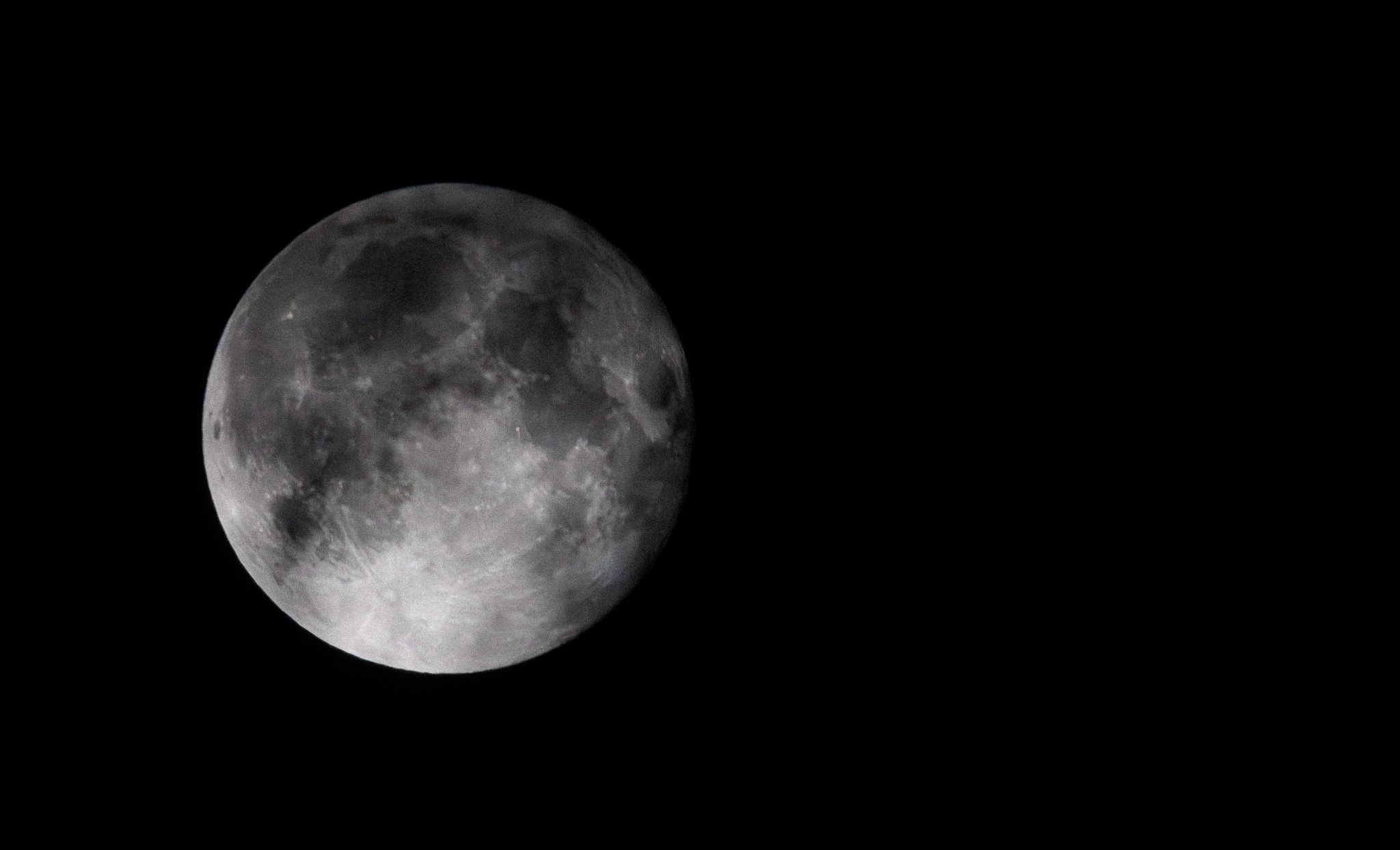 Pełnia księżyca z widocznymi kraterami i nierównościami powierzchni, sfotografowana na tle czarnego nieba.