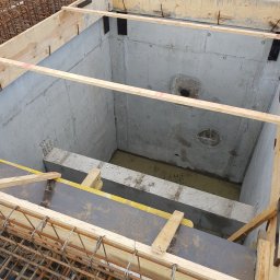 PROI Damian Borek - Betonowy zbiornik z deskowaniem i zbrojeniem, widok z góry. Wnętrze zbiornika częściowo wypełnione wodą. Widoczne elementy konstrukcyjne i detale budowlane.
