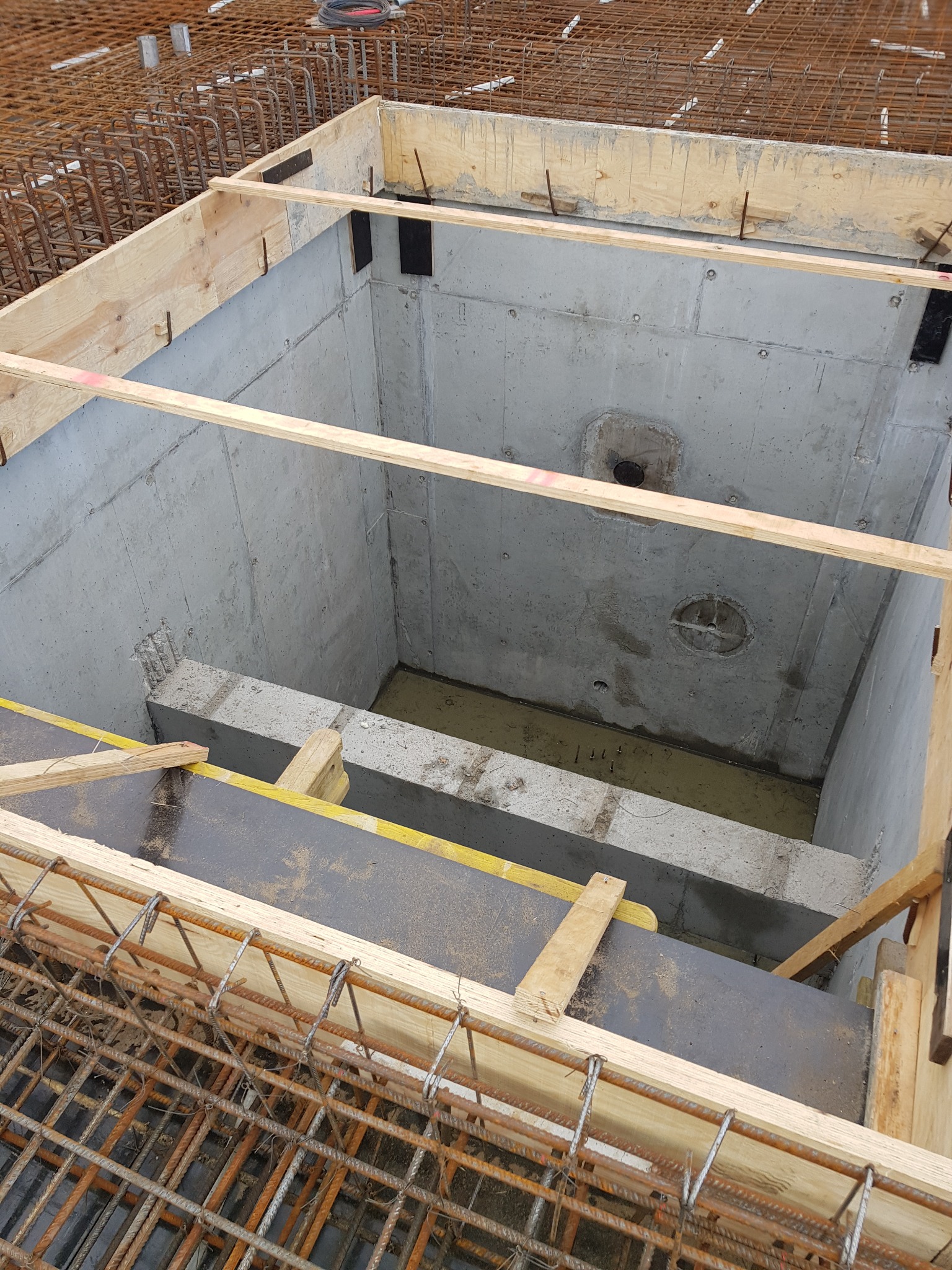 Betonowy zbiornik z deskowaniem i zbrojeniem, widok z góry. Wnętrze zbiornika częściowo wypełnione wodą. Widoczne elementy konstrukcyjne i detale budowlane.