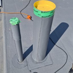 Podgórscy z wami od lat - Szary dach z papy z dwoma kominami wentylacyjnymi uszczelnionymi taśmą Siga Rissan, widoczne narzędzia i materiały izolacyjne. Prace dekarskie w toku.