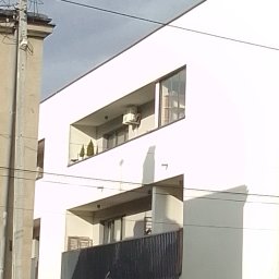 Breezo Piotr Wiśniewski - Biały budynek z balkonami; na jednym z nich widoczna jednostka zewnętrzna klimatyzacji, zieleń doniczkowa. Ujęcie z dołu, z widocznymi przewodami.