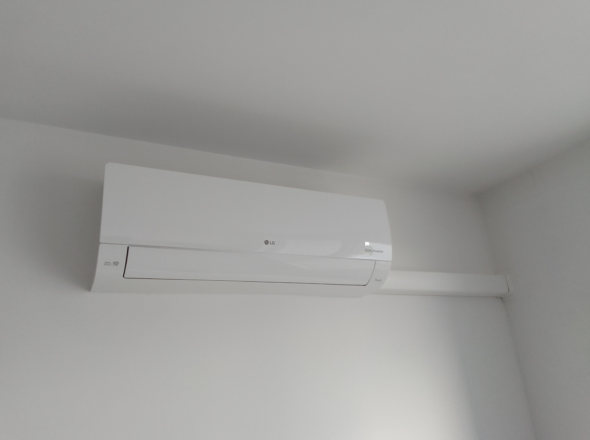 Biała klimatyzacja LG Dual Inverter zamontowana na białej ścianie, widoczny fragment rury odprowadzającej. Minimalistyczny design i czyste linie.