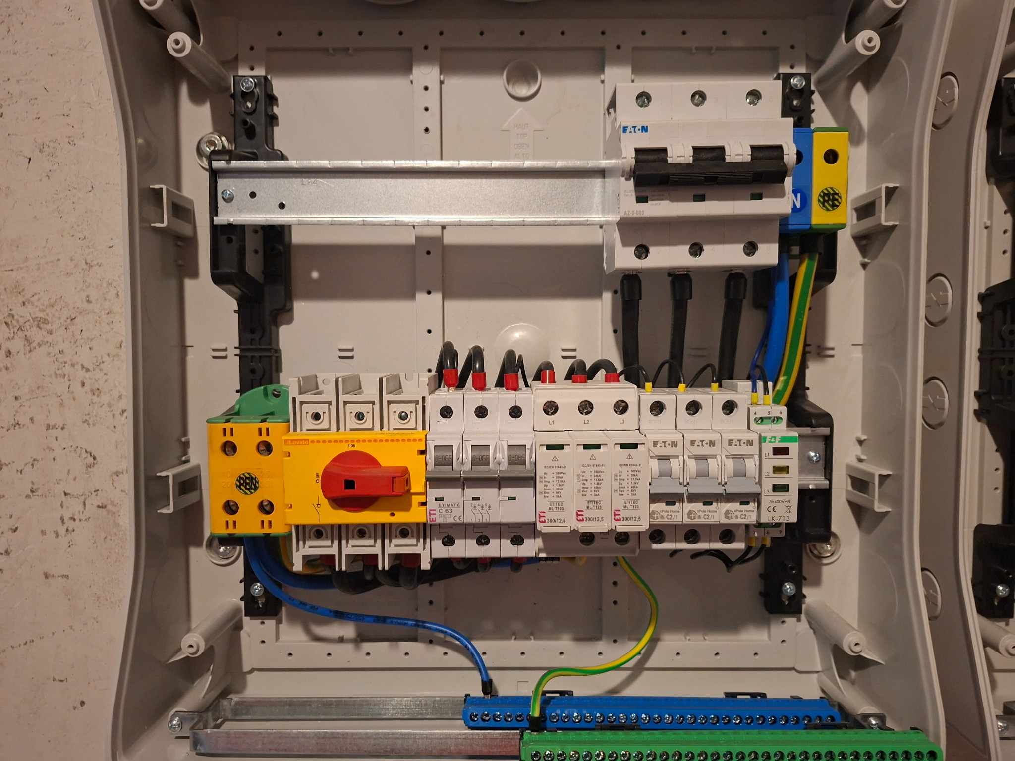 Wnętrze skrzynki rozdzielczej z zamontowanymi bezpiecznikami, wyłącznikami i listwami zaciskowymi, uporządkowane przewody. Widoczne elementy marki Eaton i Lovato.