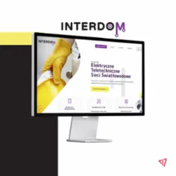 Monitor wyświetlający stronę internetową firmy Interdom prezentującą instalacje elektryczne, teletechniczne i światłowodowe, z żółtym kaskiem i rękawicą w tle