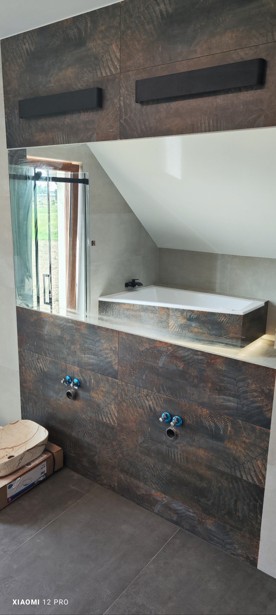 Nowoczesna łazienka na poddaszu z brązowymi płytkami imitującymi drewno z motywem paproci, białą wanną i umywalką z kamienia na kartonie