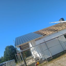 USŁUGI BUDOWLANE ARKADIUSZ PESTKA - Dom w trakcie wymiany pokrycia dachowego, widoczne rusztowania, częściowo położona blacha trapezowa i więźba dachowa pod błękitnym niebem.
