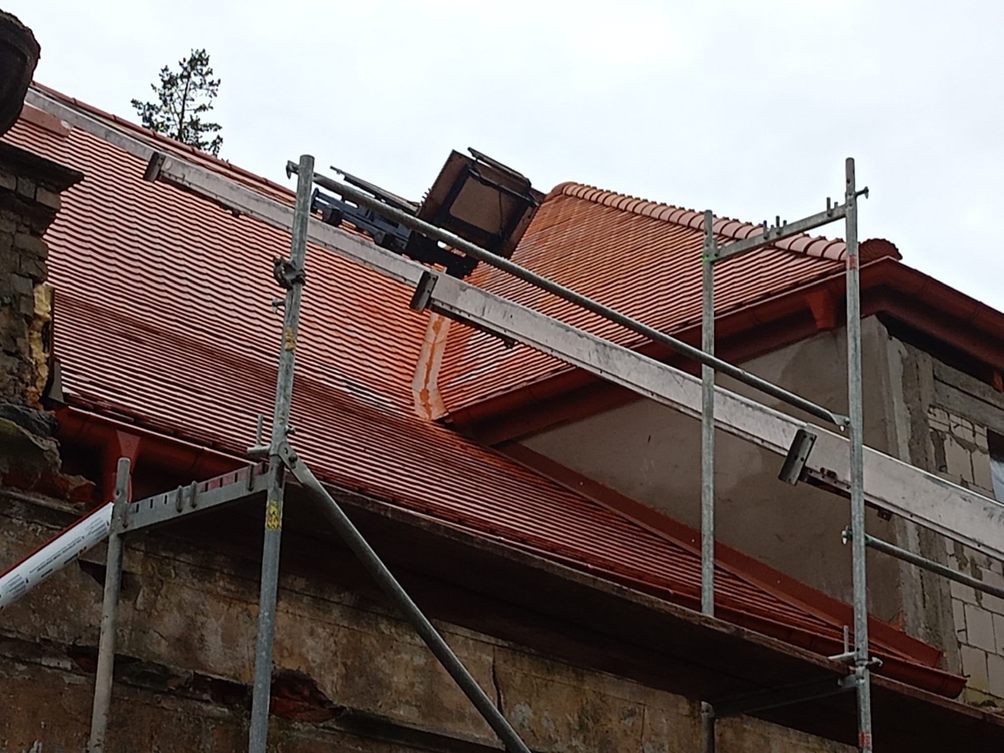 Czerwona dachówka karpiówka na zabytkowym budynku w trakcie prac dekarskich, widoczne rusztowanie i podnośnik dekarski.