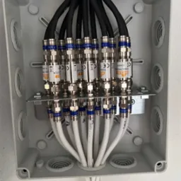 Rozdzielnica elektryczna z licznymi kablami koncentrycznymi i złączami F, zamontowana na ścianie, widoczne etykiety na złączach.