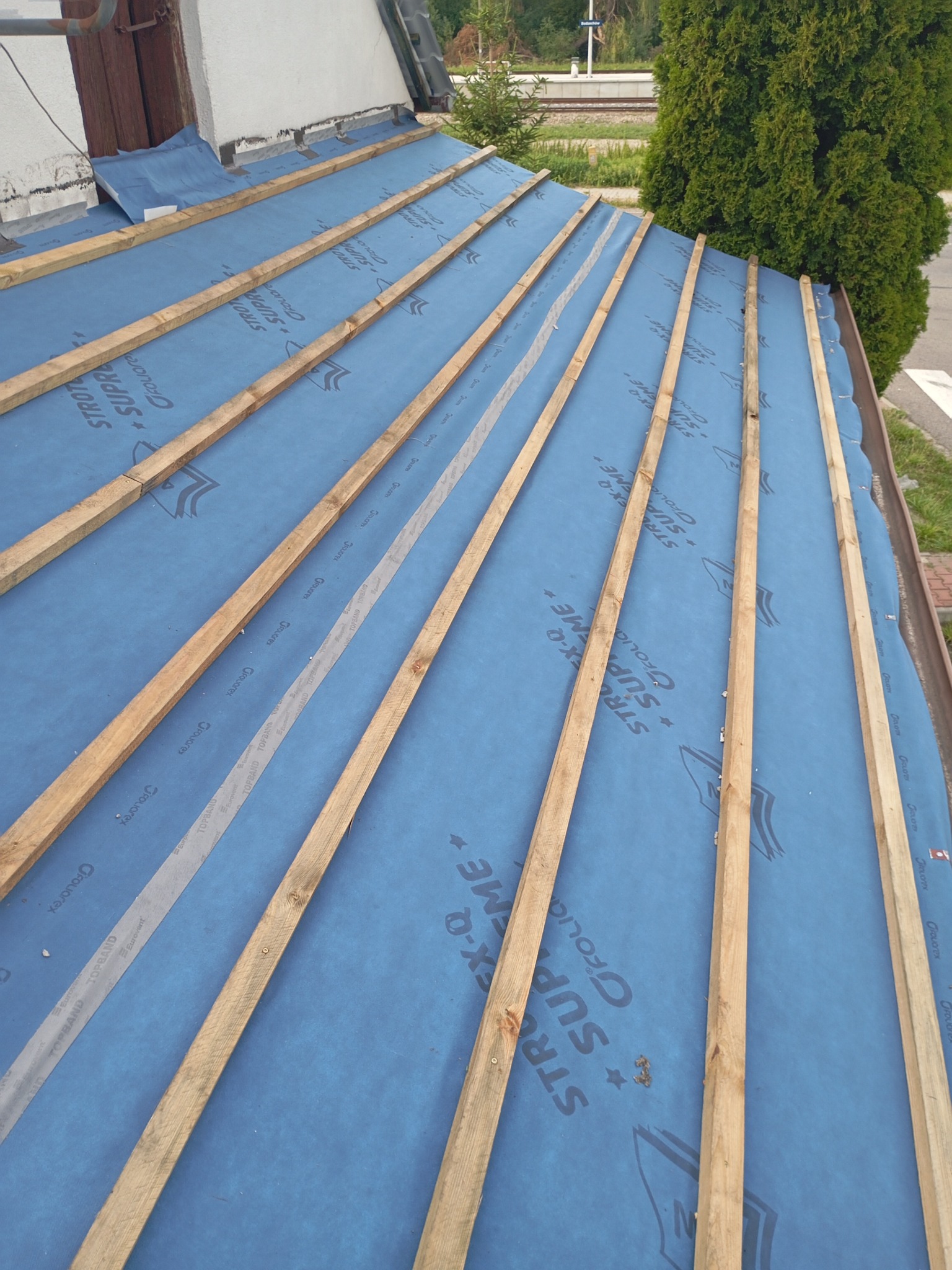 Niebieska membrana dachowa z drewnianymi łatami, przygotowana pod pokrycie dachowe, widok z góry.