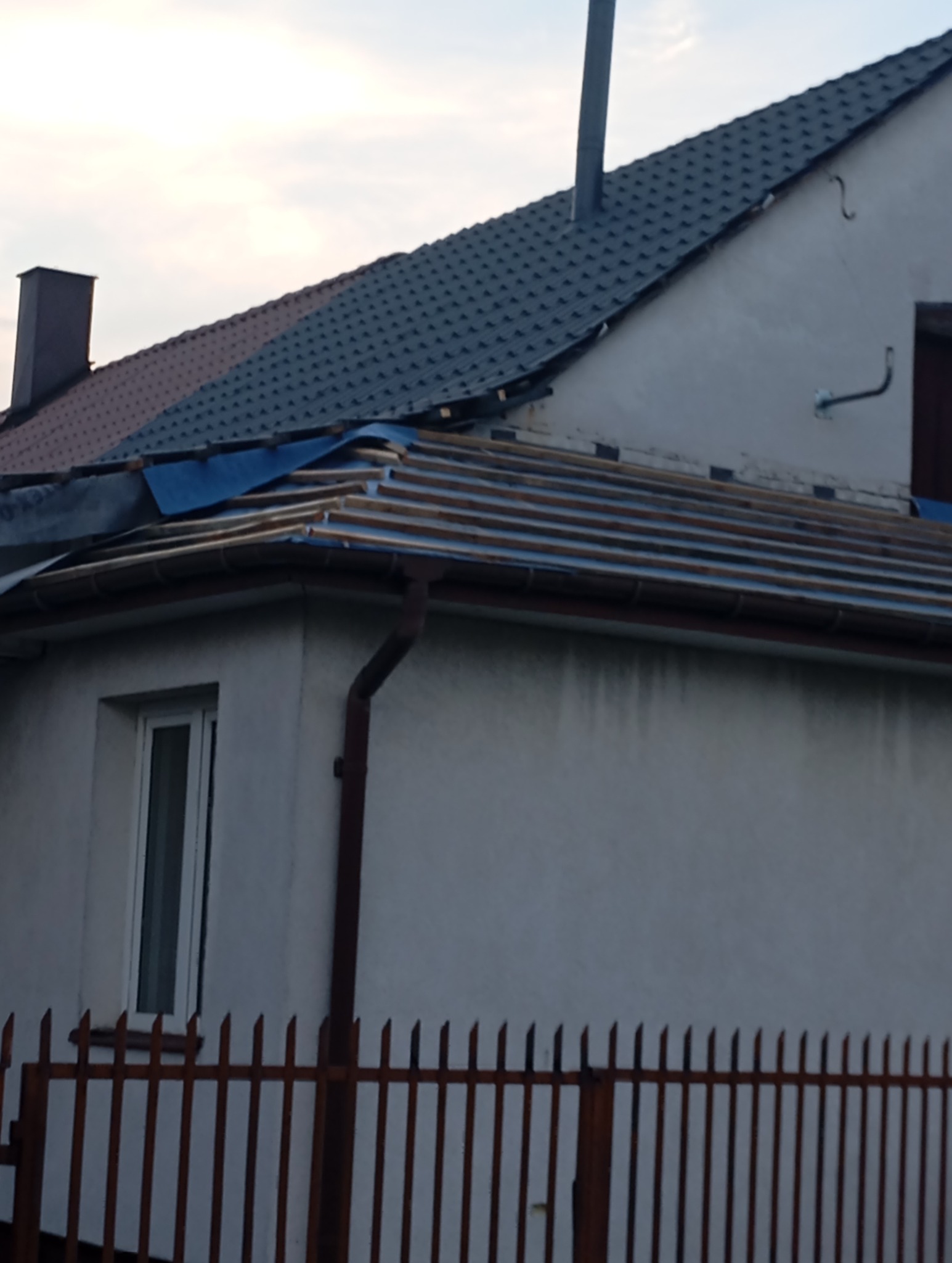 Dom w trakcie wymiany pokrycia dachowego, widoczne drewniane łaty i fragmenty nowej dachówki