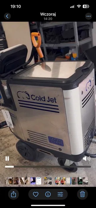 Urządzenie Cold Jet do czyszczenia suchym lodem, widoczne logo i dysza z pomarańczową rączką, na tle półek warsztatowych.
