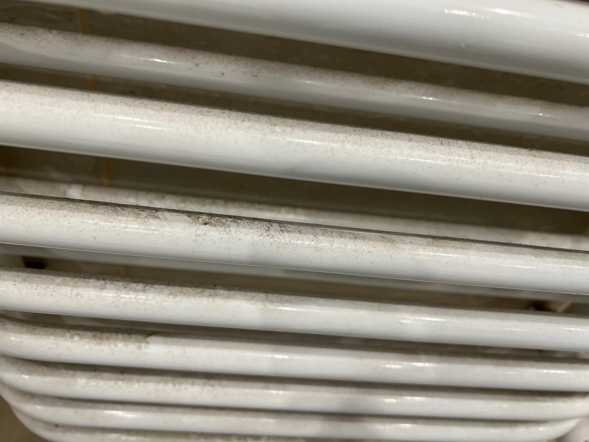 Biały, żebrowany grzejnik pokryty kurzem i zabrudzeniami, widoczne ślady użytkowania.