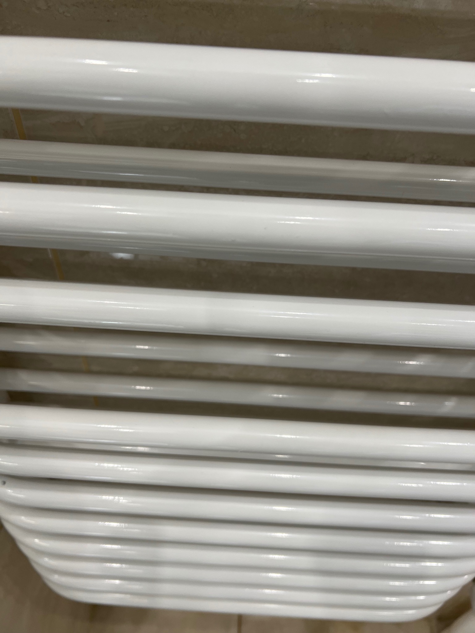 Biały, drabinkowy grzejnik łazienkowy, żebrowany, zamontowany na beżowej ścianie, widok z bliska.