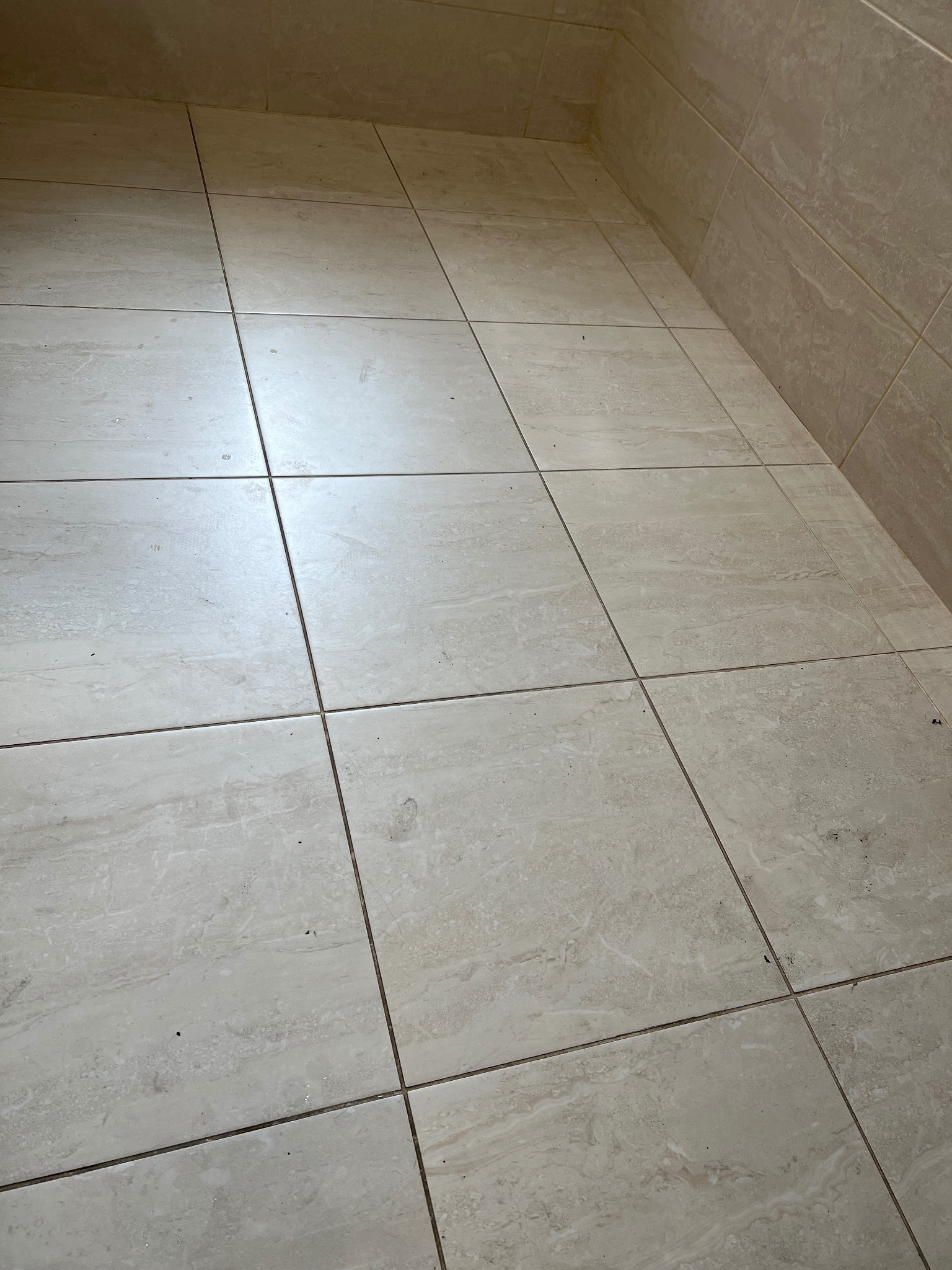 Beżowe płytki podłogowe i ścienne z ciemniejszymi fugami, widoczne drobne zabrudzenia.