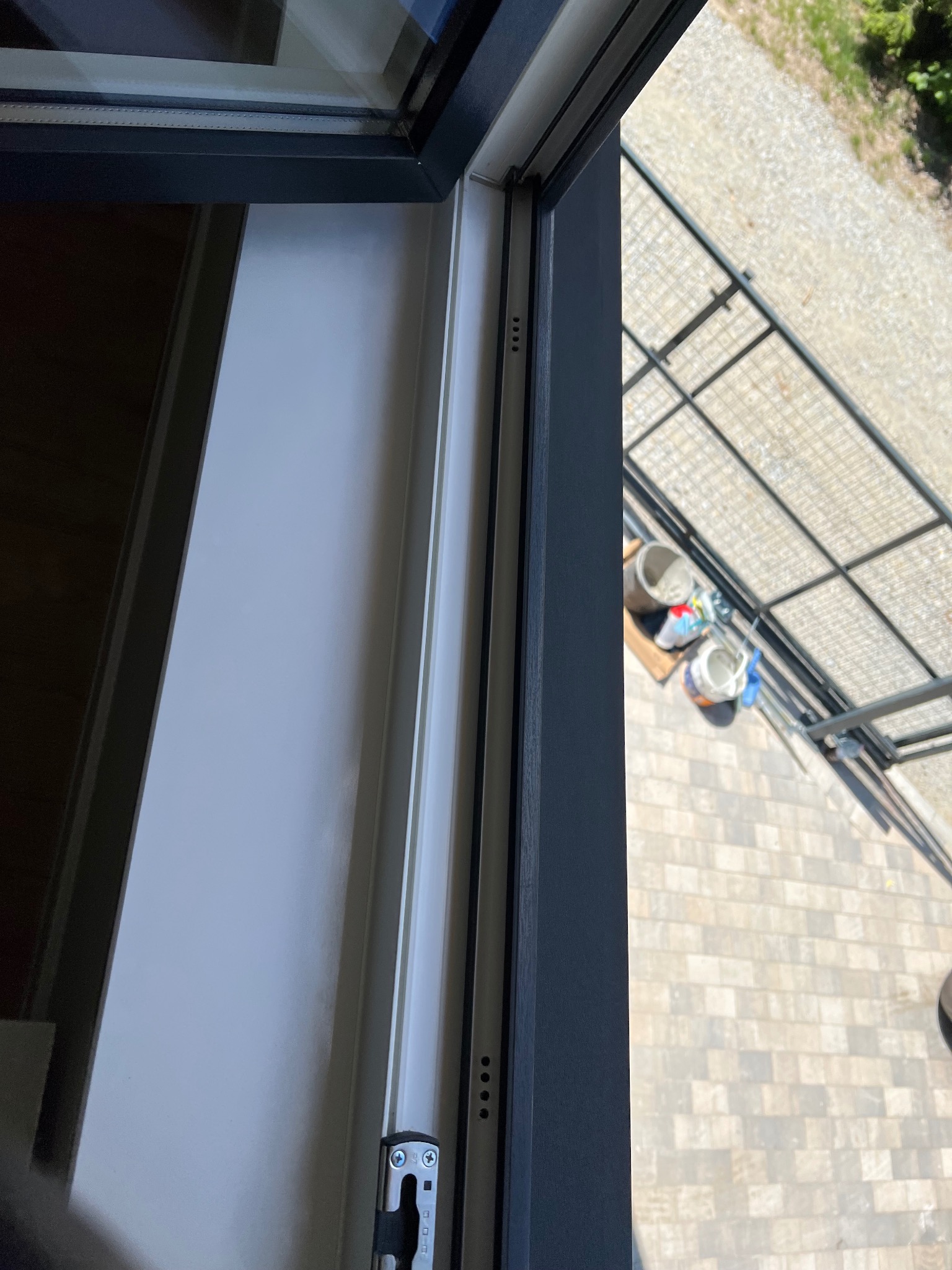 Wnętrze okna PCV po umyciu, z widokiem na zewnątrz. Czysta szyba i rama bez smug. Na zewnątrz widoczny taras i akcesoria do sprzątania.