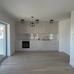 Robert Nowak - Jasna, nowoczesna kuchnia z marmurowym backsplashiem i drewnianą podłogą. Minimalistyczne, czarne lampy wiszące dopełniają aranżację. Duże okno balkonowe wpuszcza naturalne światło.