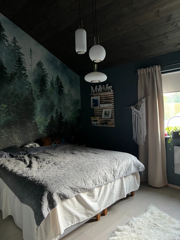 Sypialnia z fototapetą leśną, ciemną drewnianą boazerią sufitową i trzema nowoczesnymi lampami wiszącymi.