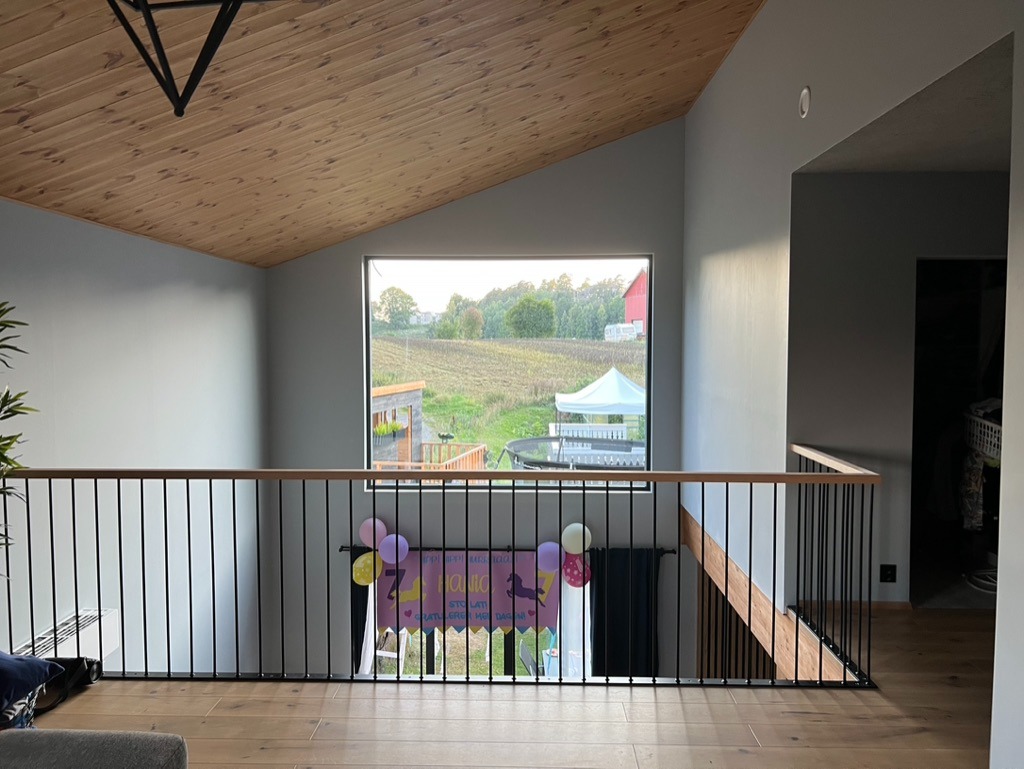 Nowoczesne wnętrze domu z drewnianym sufitem i balustradą. Widok na krajobraz przez okno. Dekoracje urodzinowe dodają koloru.