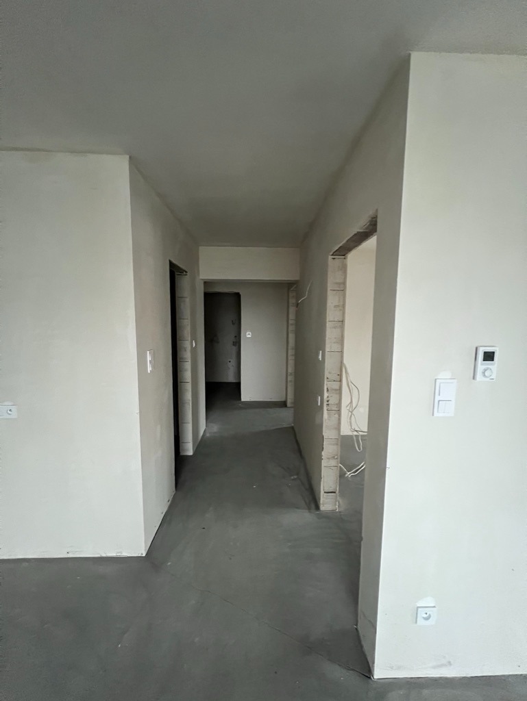 Surowy stan mieszkania w trakcie remontu: gładzie na ścianach, wylewka podłogowa, widoczne kable elektryczne. Przygotowanie do dalszych prac wykończeniowych.