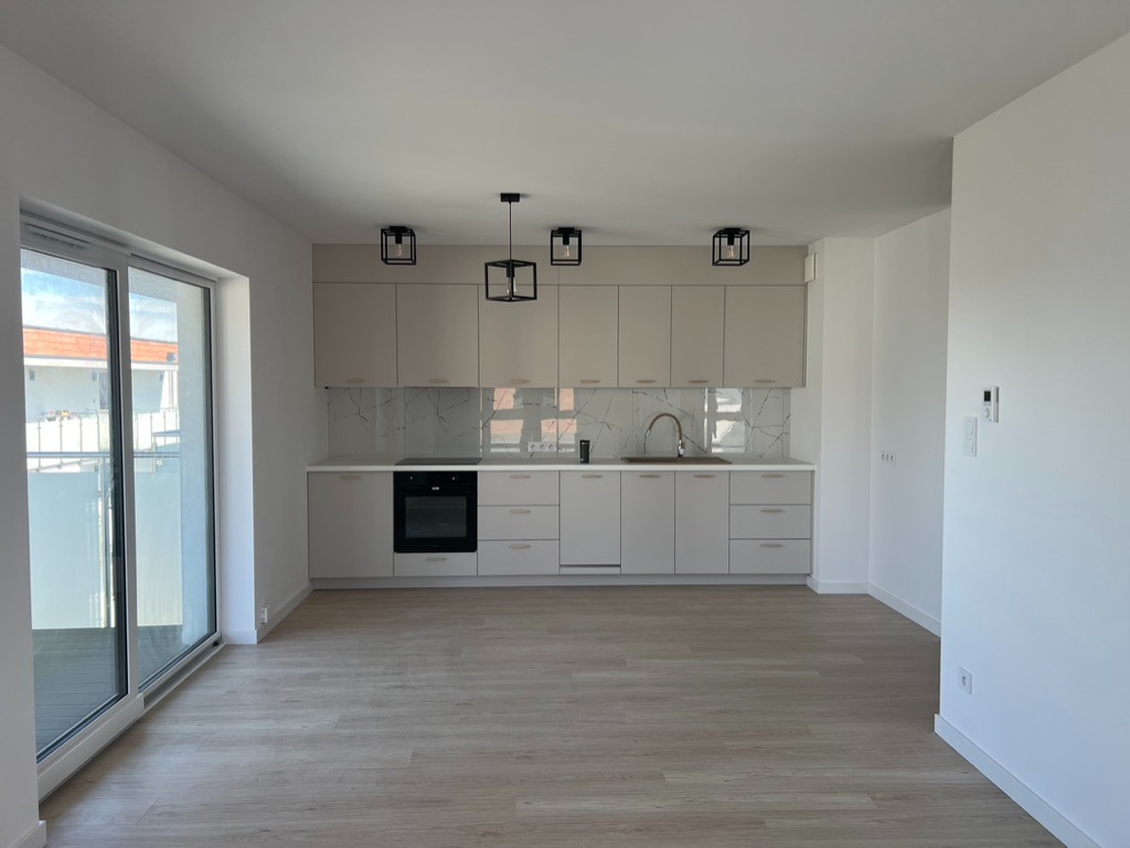 Jasna, nowoczesna kuchnia z marmurowym backsplashiem i drewnianą podłogą. Minimalistyczne, czarne lampy wiszące dopełniają aranżację. Duże okno balkonowe wpuszcza naturalne światło.