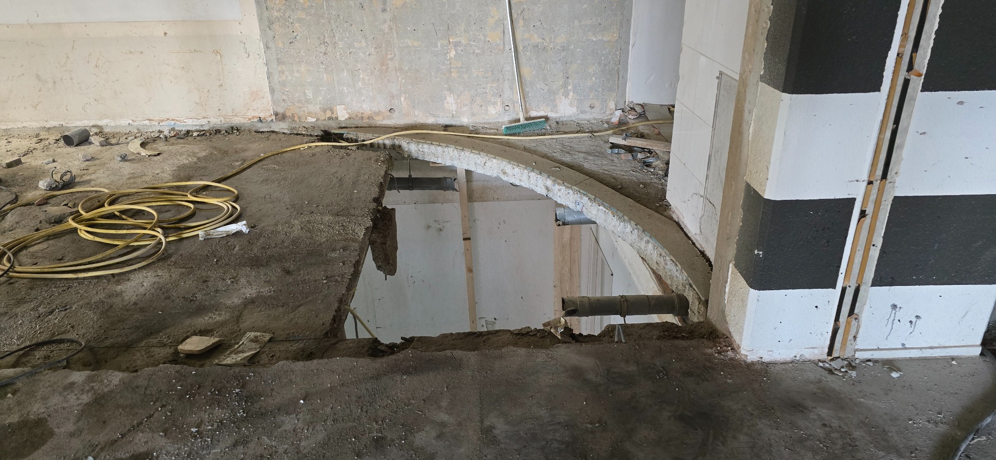 Fragment podłogi po wyburzeniu ściany, widoczne przewody elektryczne, gruz i odsłonięta konstrukcja stropu.