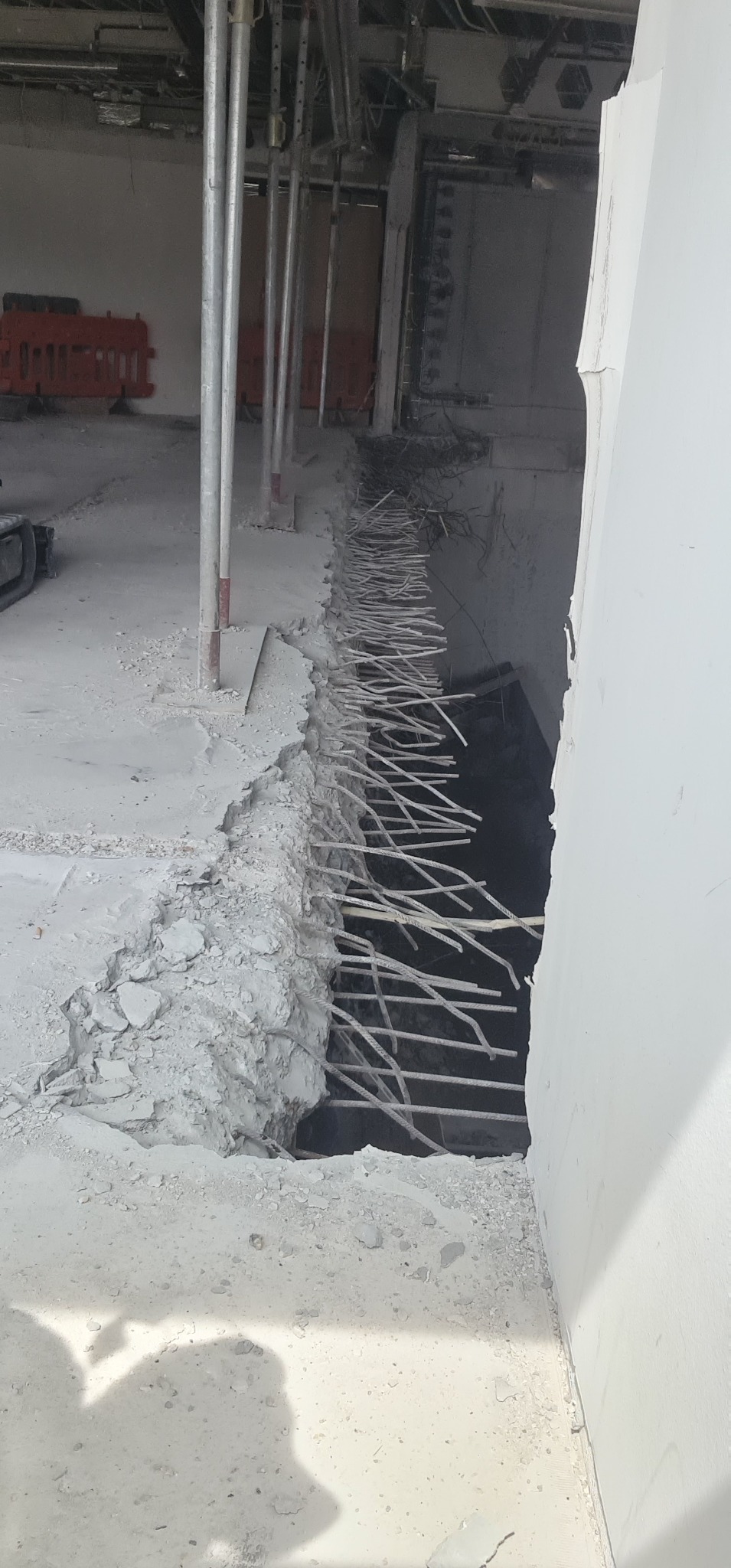 Wykucie otworu w żelbetowej ścianie z wystającymi prętami zbrojeniowymi, widoczne podpory szalunkowe i gruz.