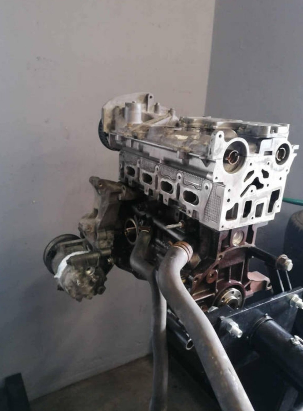 Zdemontowany silnik samochodowy na stojaku warsztatowym. Widoczne elementy układu chłodzenia i głowica silnika. Szary odcień tła.