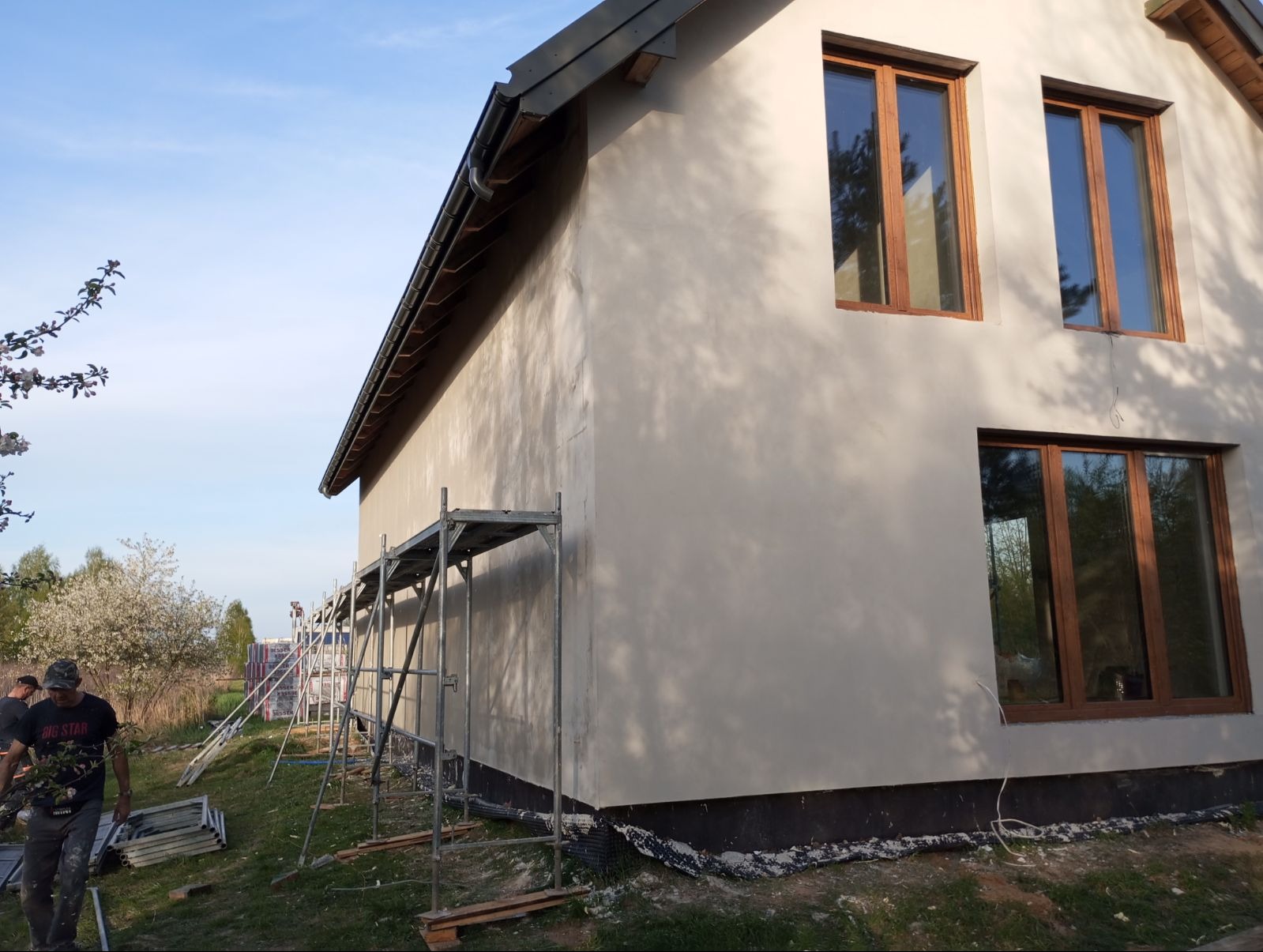 Świeżo otynkowana elewacja domu w Kowalu, z widocznymi drewnianymi ramami okiennymi i rusztowaniem, przygotowana do dalszych prac wykończeniowych.