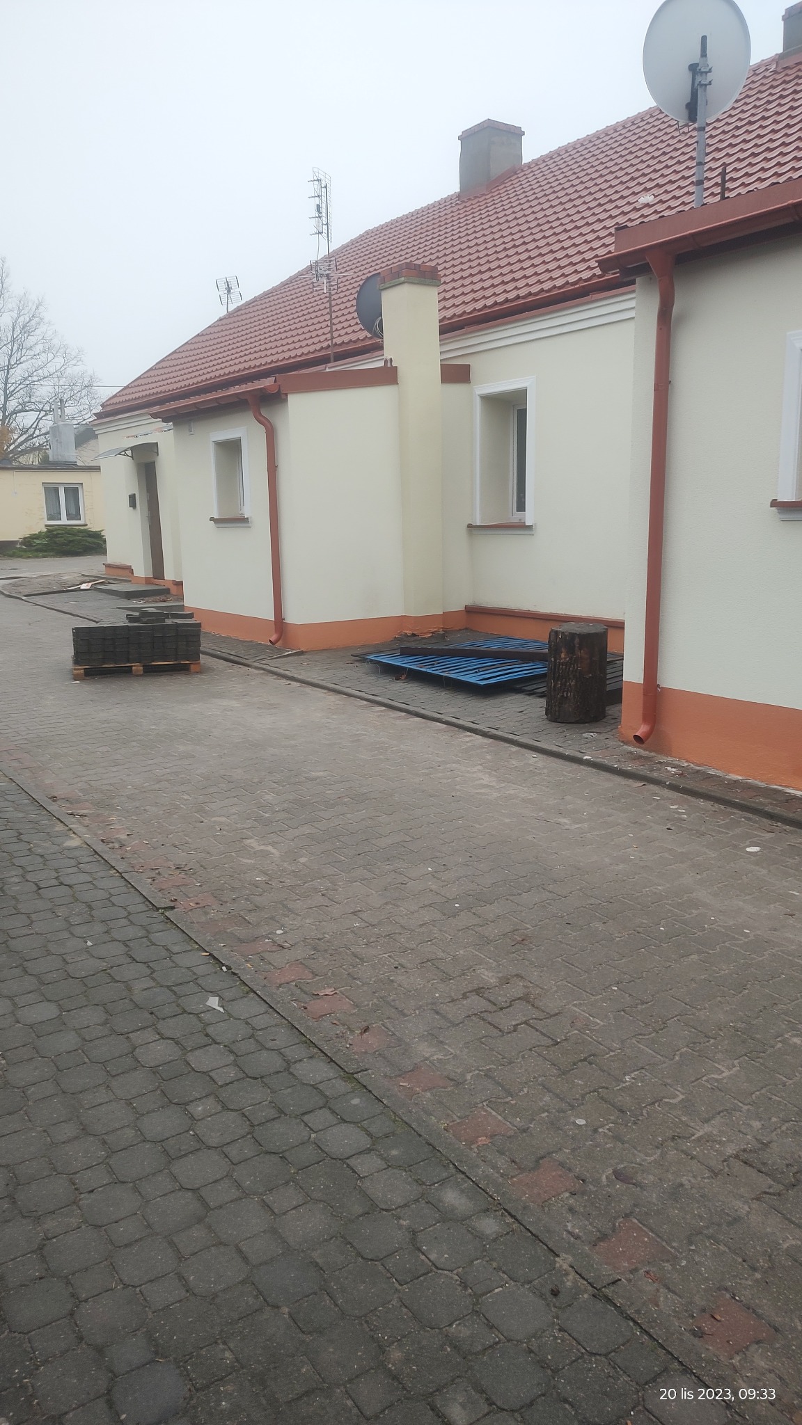 Budynek jednorodzinny po remoncie elewacji, widoczne nowe tynki i pomalowane detale architektoniczne, na pierwszym planie kostka brukowa i paleta z kostką.
