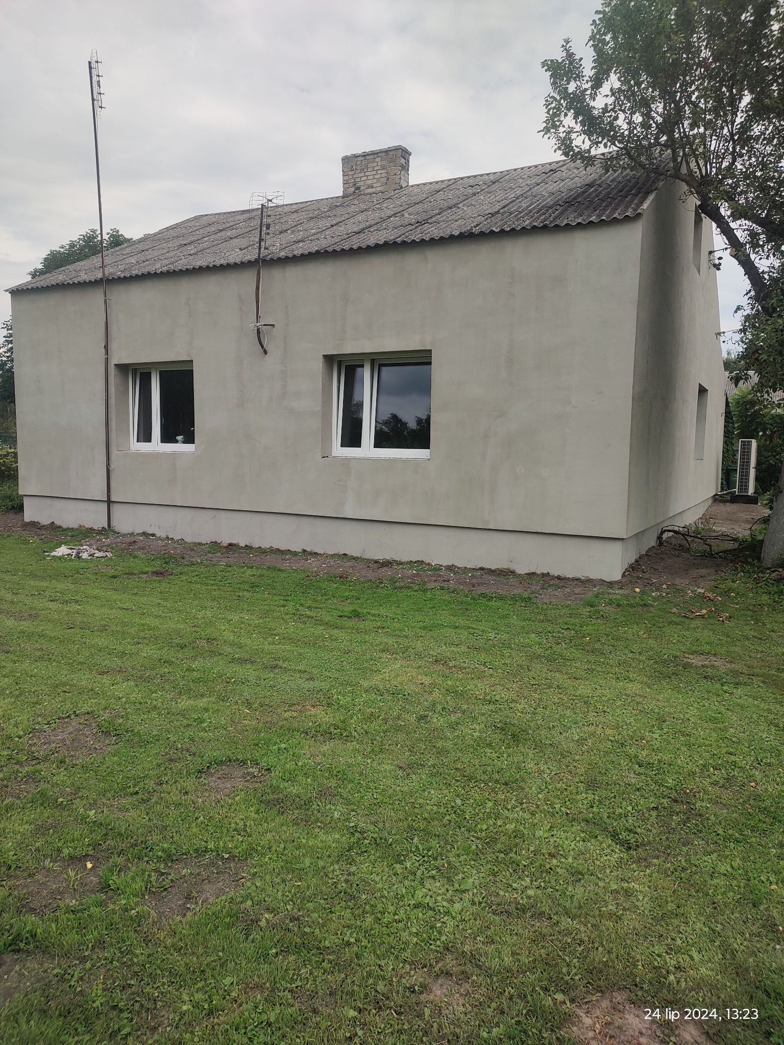 Dom jednorodzinny z nową, szarą elewacją, widoczne dwie białe okna, antena na dachu i trawnik z przodu budynku.