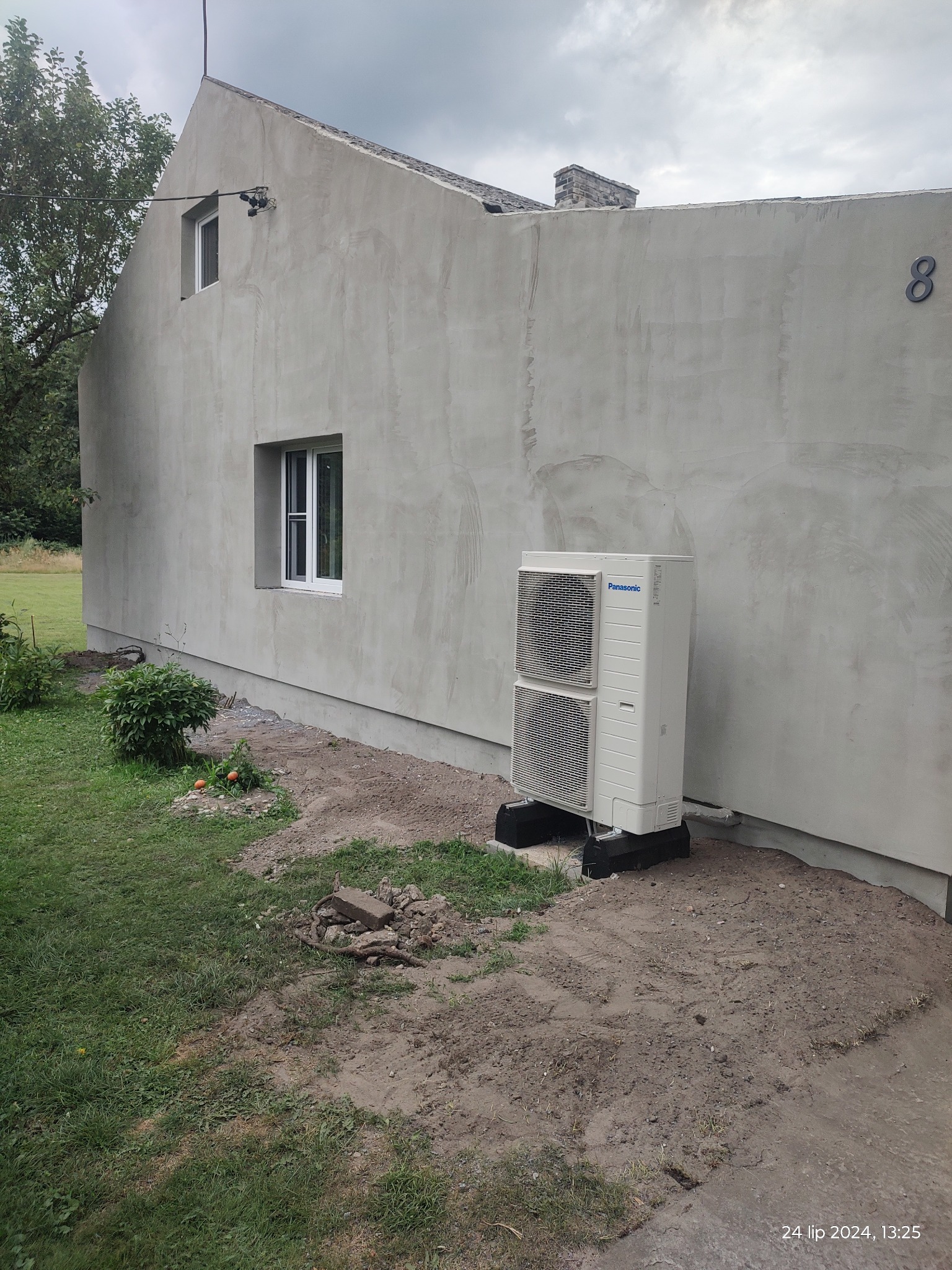 Świeżo otynkowana elewacja domu z zamontowaną zewnętrzną jednostką klimatyzacji Panasonic i widocznym numerem posesji '8'.