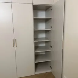 Jasna, nowoczesna szafa wnękowa z otwartymi drzwiami, ukazującymi puste półki; widoczny fragment parkietu ułożonego w jodełkę.