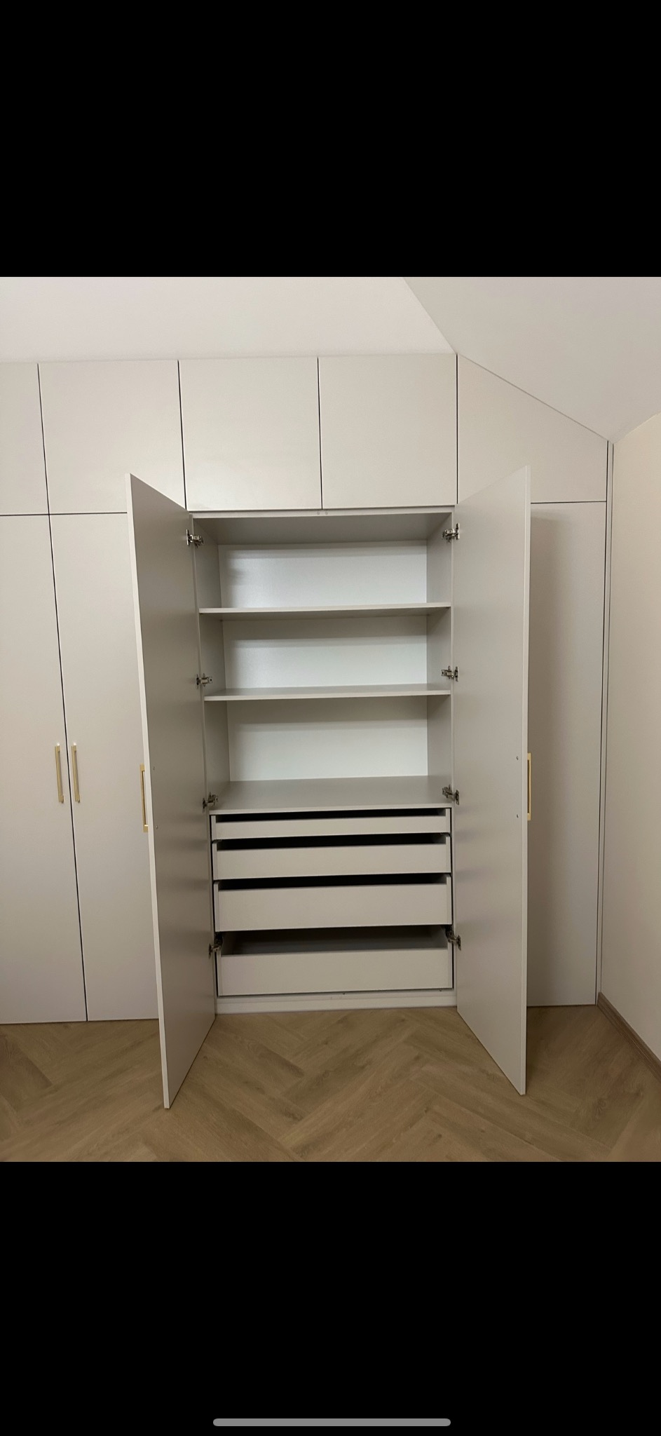 Jasna szafa wnękowa z otwartymi drzwiami, widoczne półki i szuflady, minimalistyczny design, parkiet w jodełkę na podłodze.