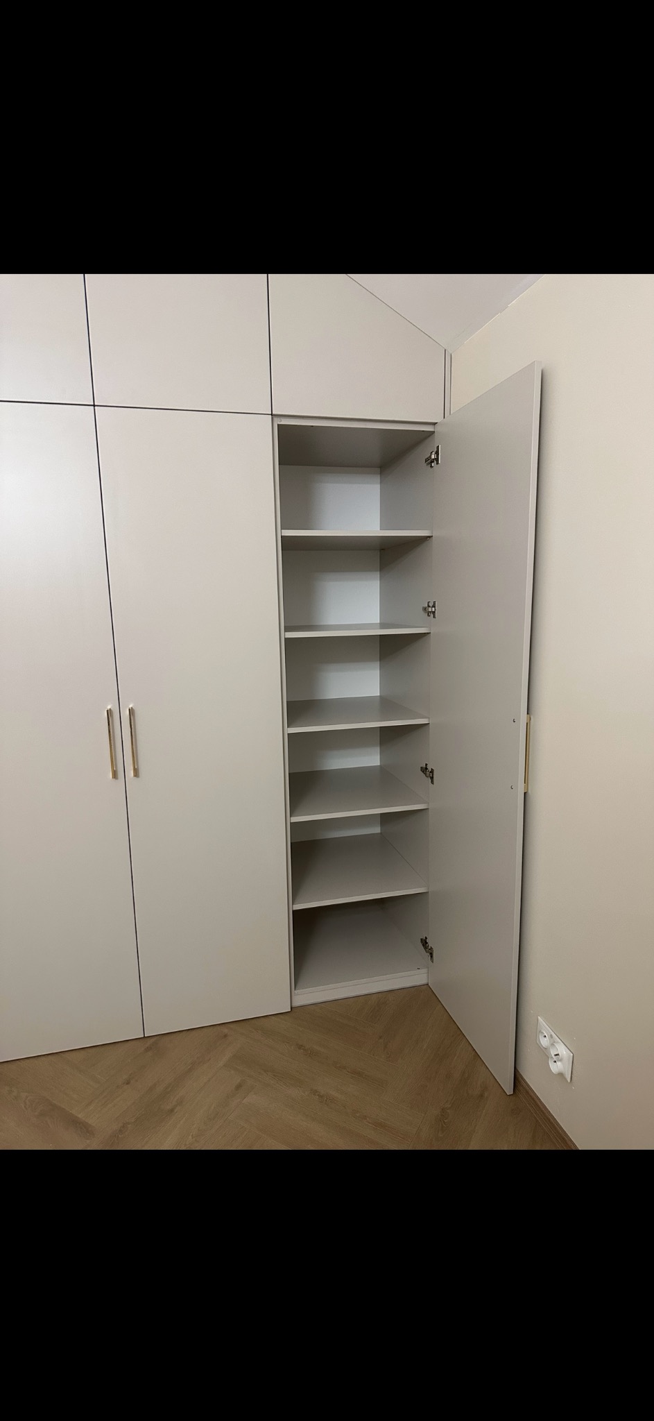 Jasna, nowoczesna szafa wnękowa z otwartymi drzwiami, ukazującymi puste półki; widoczny fragment parkietu ułożonego w jodełkę.