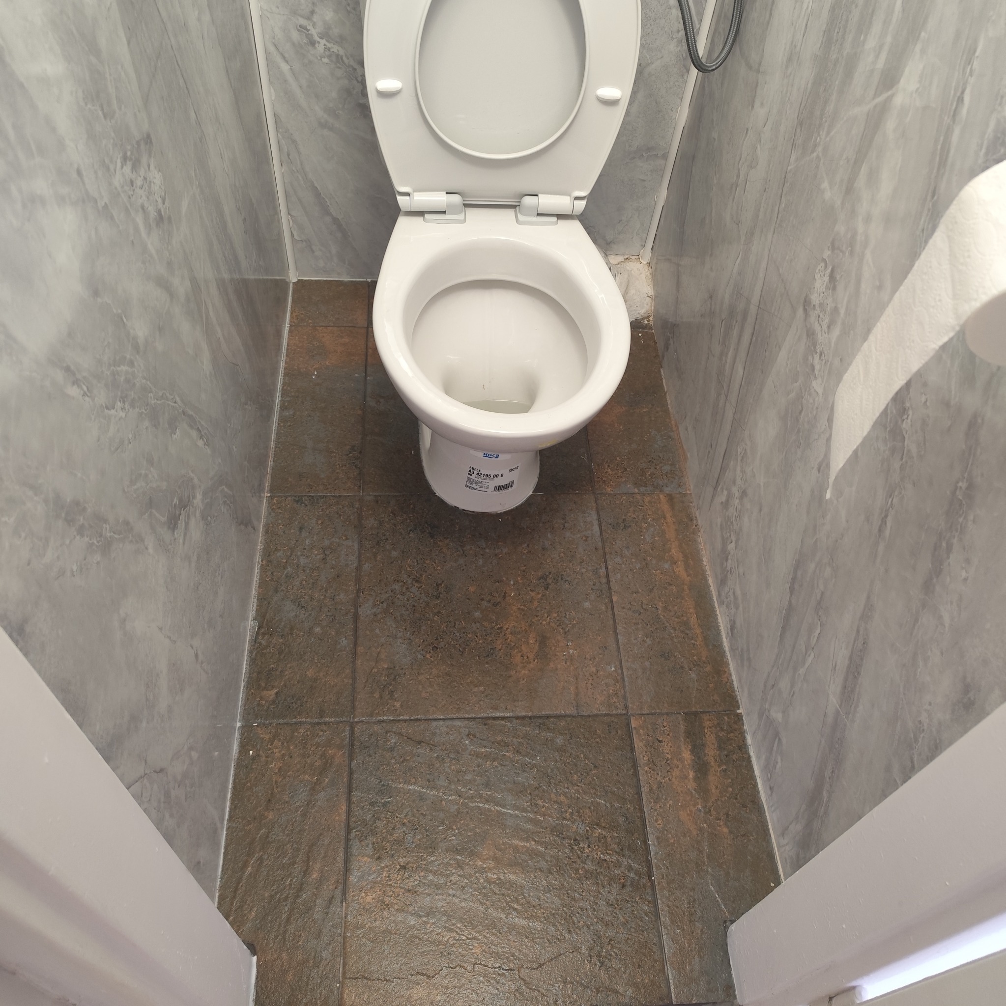 Toaleta z otwartą klapą, brązowe płytki podłogowe i marmurowe ściany. Widok z góry na czystą toaletę w łazience.