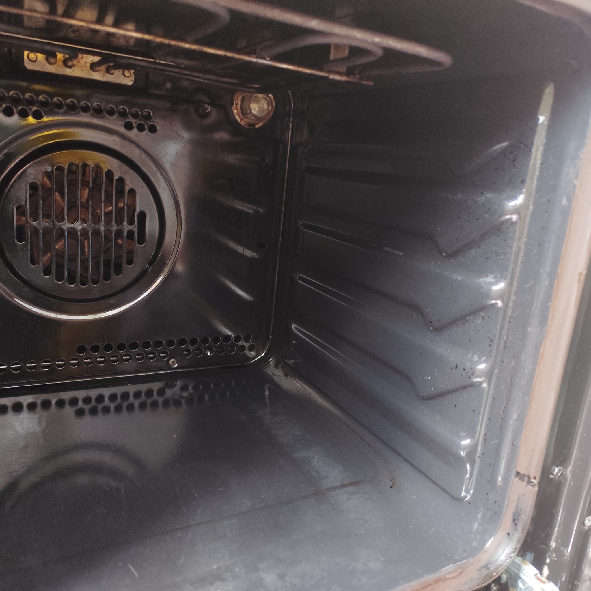 Wnętrze brudnego piekarnika z widocznymi resztkami jedzenia i tłuszczu na ściankach i dnie. Metalowa obudowa z otworami wentylacyjnymi.